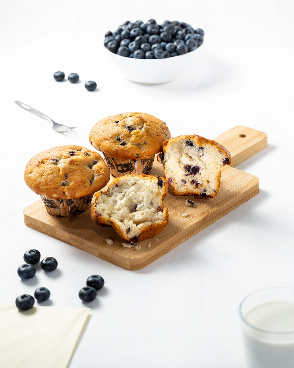 Blueberry muffins on a wooden cutting board with fresh blueberries around.