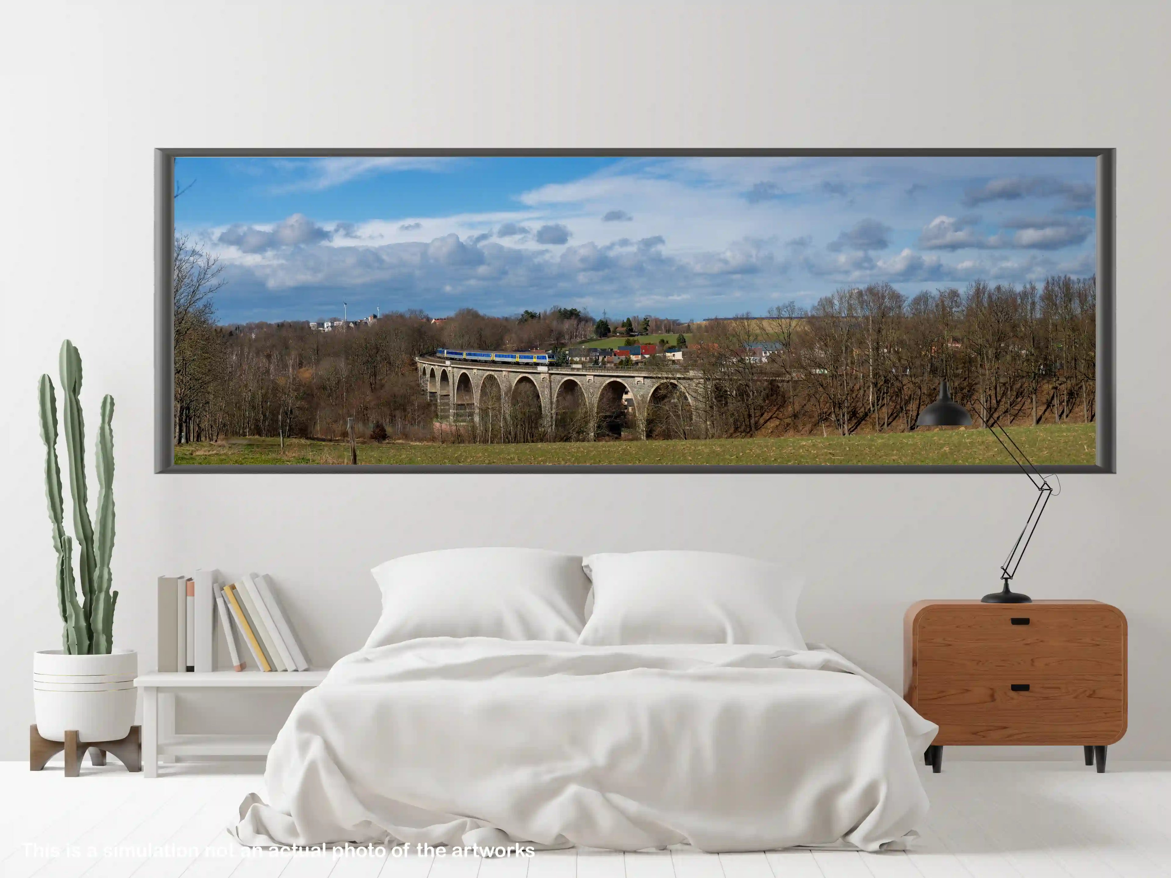 Framed panoramic landscape of a viaduct with a train, displayed above a bed in a bedroom.