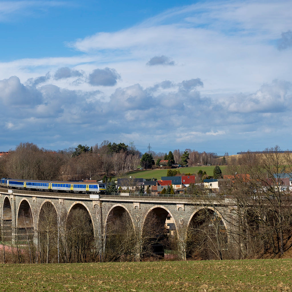 Train crossing a stone viaduct with a scenic landscape and blue sky.