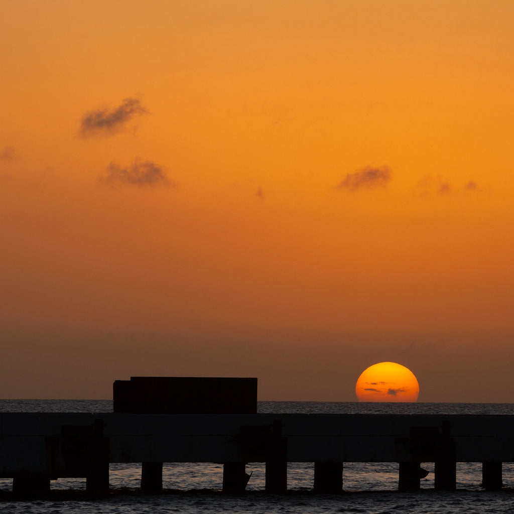 Sunset over water with silhouette of a pier