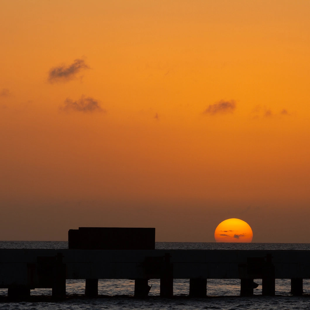 Sunset over water with silhouette of a pier