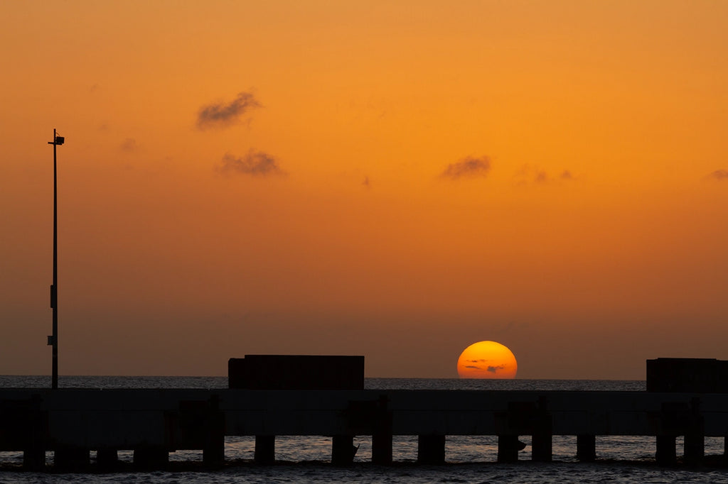 Sunset over water with silhouette of a pier