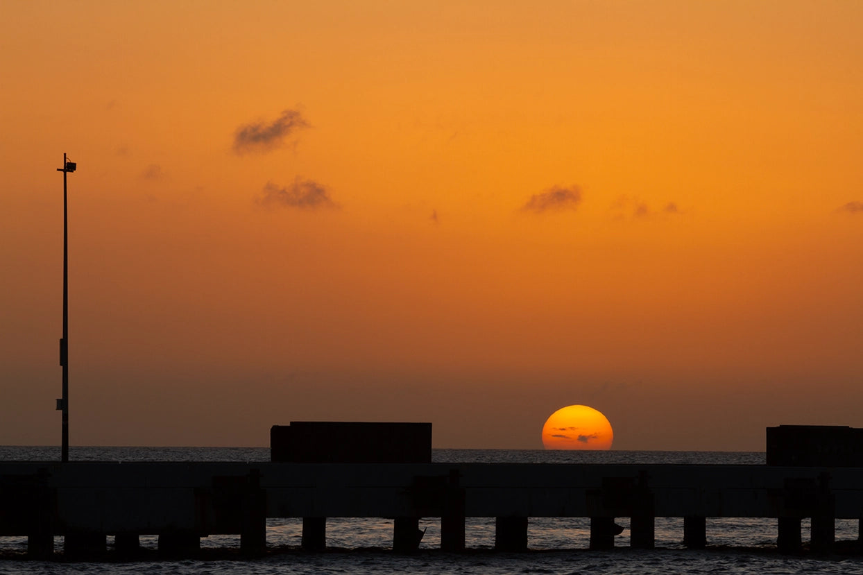 Sunset over water with silhouette of a pier