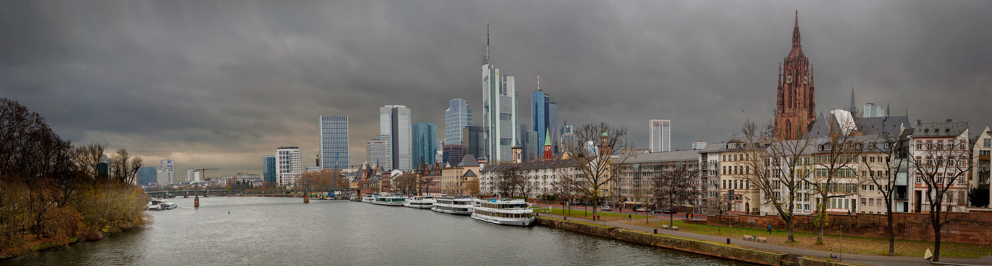 Panoramic view of Frankfurt. The towering skyscrapers of the financial district rise dramatically into the stormy sky, while the Gothic spires of the Frankfurt Cathedral remind us of the city’s deep historical roots. Actual format of the artwork.