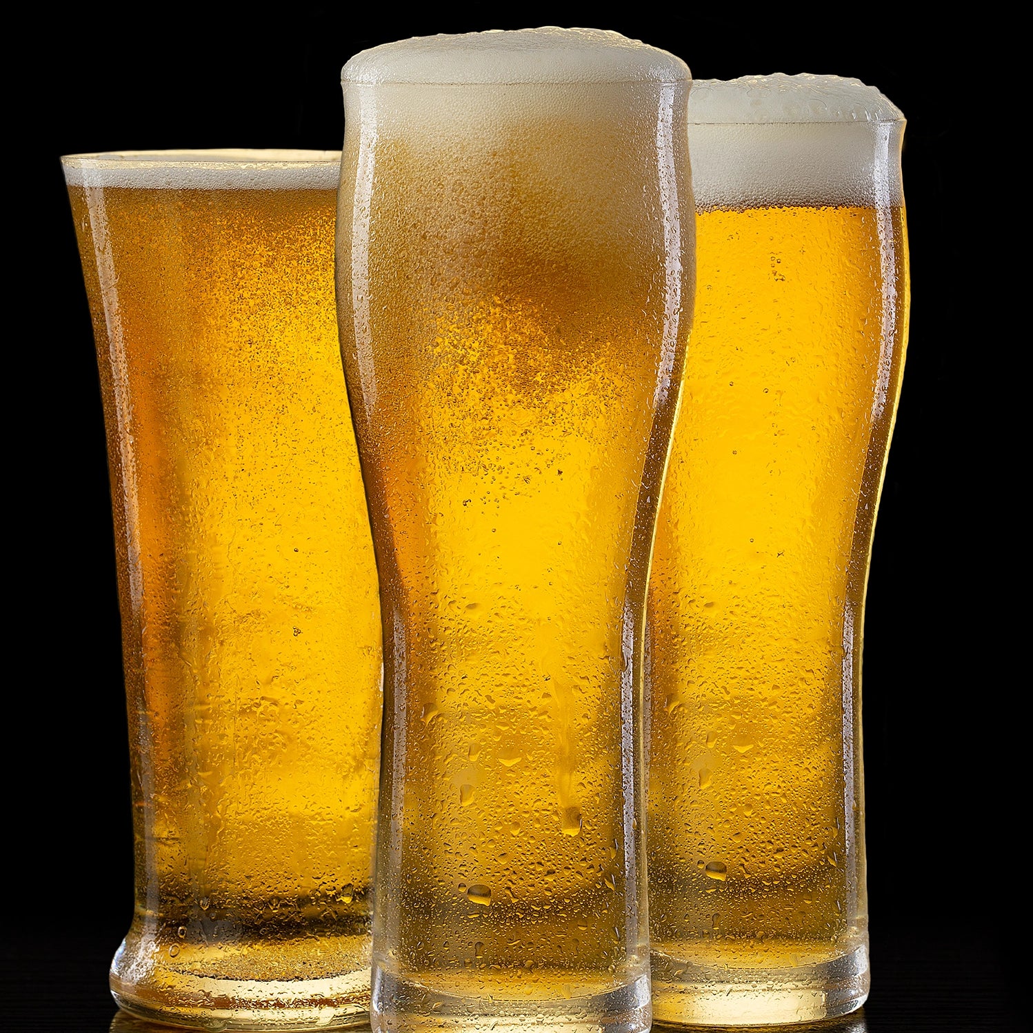 Three glasses of beer with foam on a black background