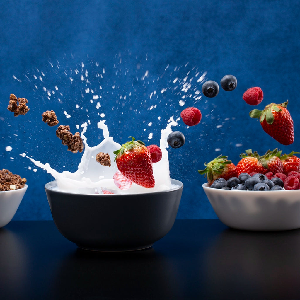 Bowl of fruit with milk splash against a blue background