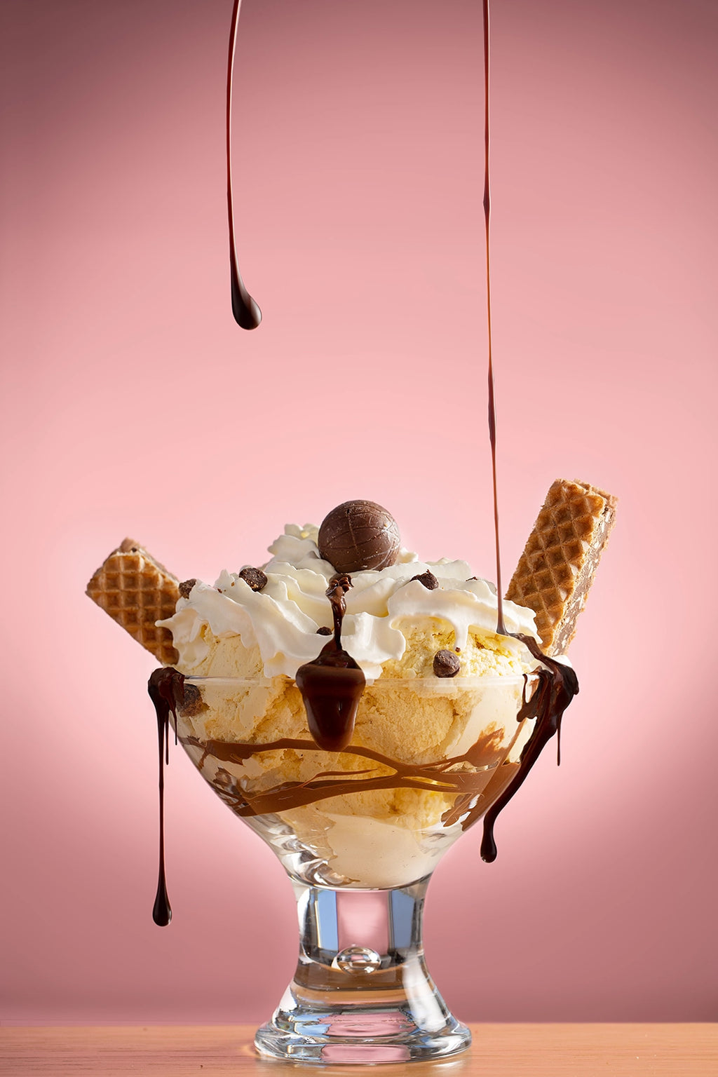 Ice cream sundae with waffles, chocolate sauce, and whipped cream on a pink background