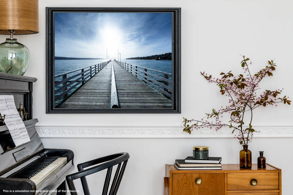 Framed photograph of a dock on a wall above a piano in a room with a wooden cabinet and plant.