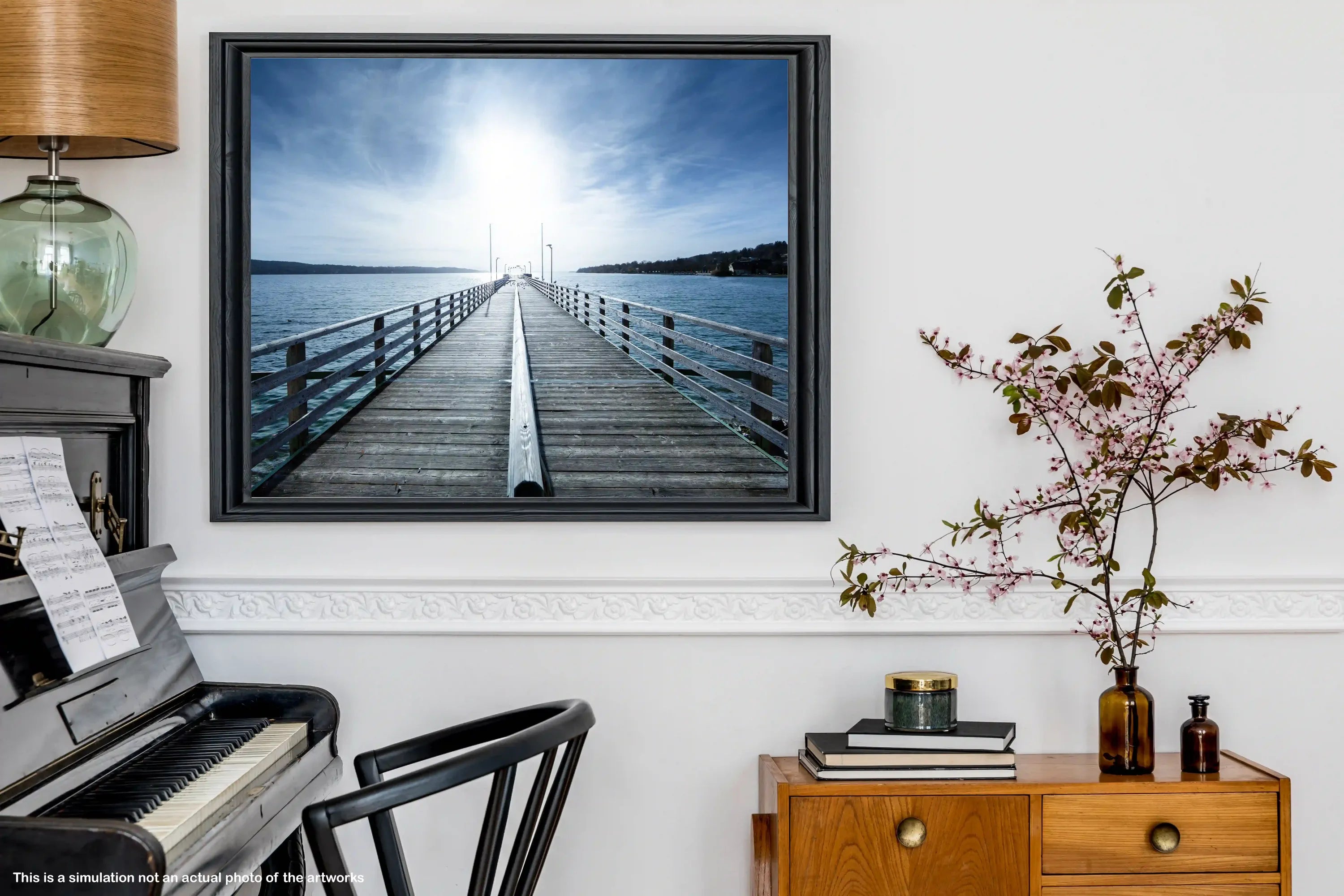 Framed photograph of a dock on a wall above a piano in a room with a wooden cabinet and plant.