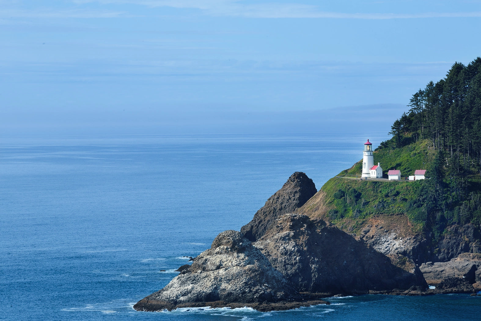 Lighthouse on a rocky outcrop with blue ocean and clear sky