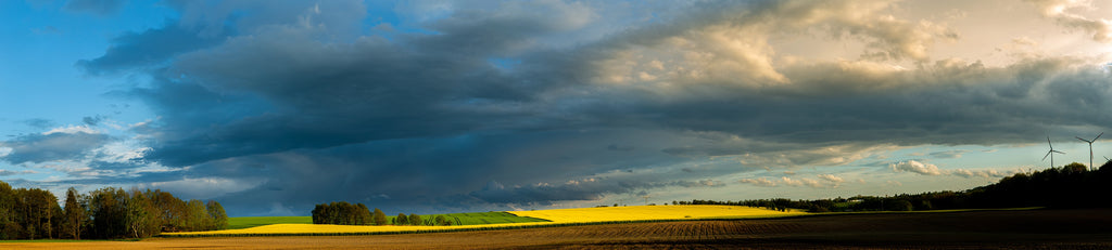 Panoramic view of a field with a dramatic sky filled with clouds.