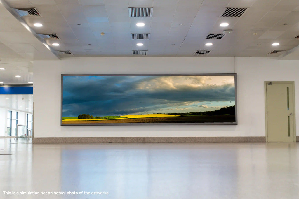 Large panoramic wall art of a landscape with blue sky and clouds in a modern hallway.