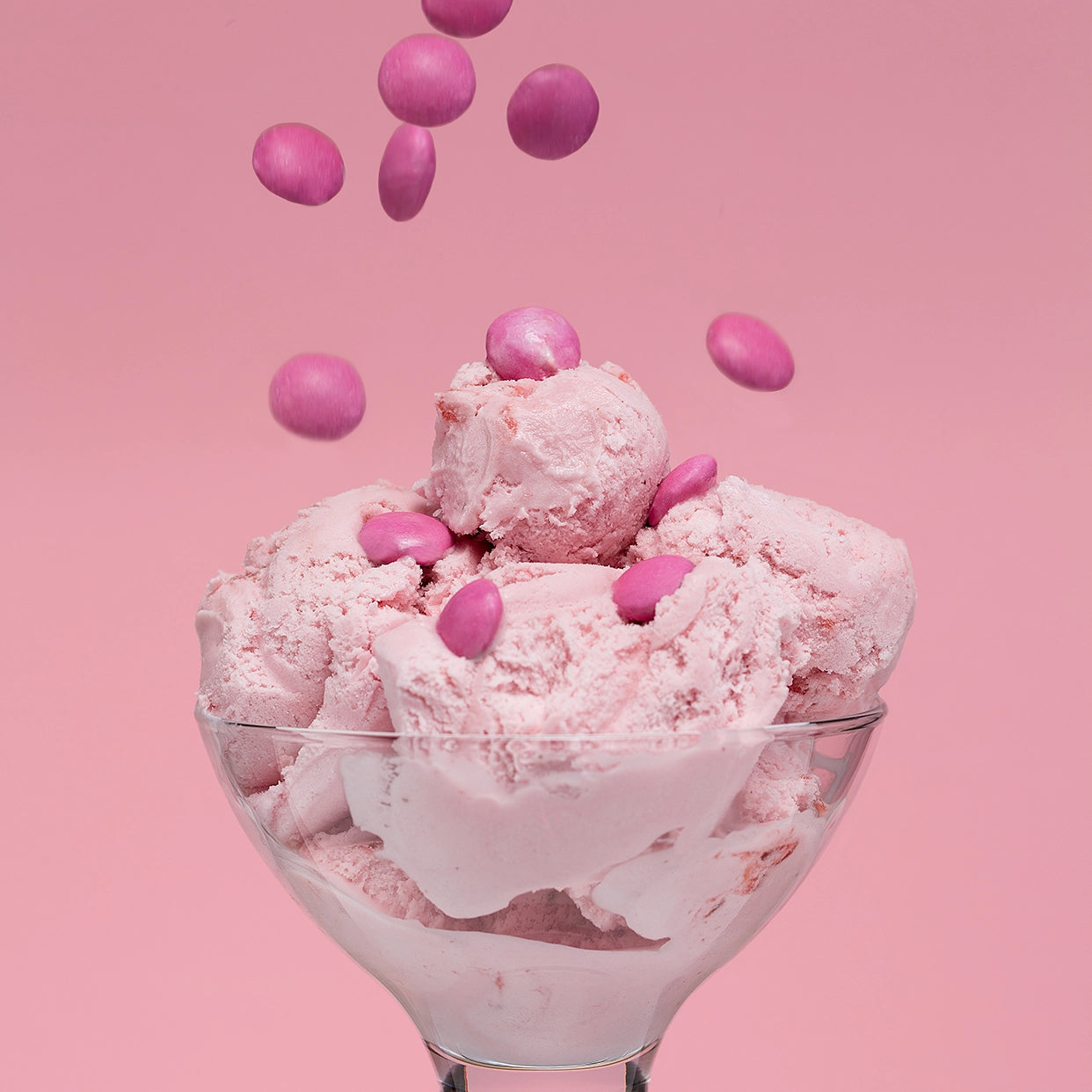 Pink ice cream with pink candies in a glass bowl on a pink background
