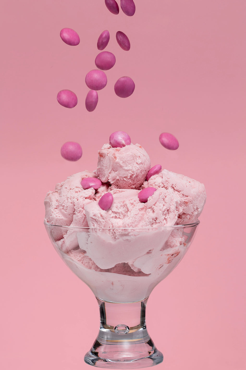 Pink ice cream with pink candies in a glass bowl on a pink background