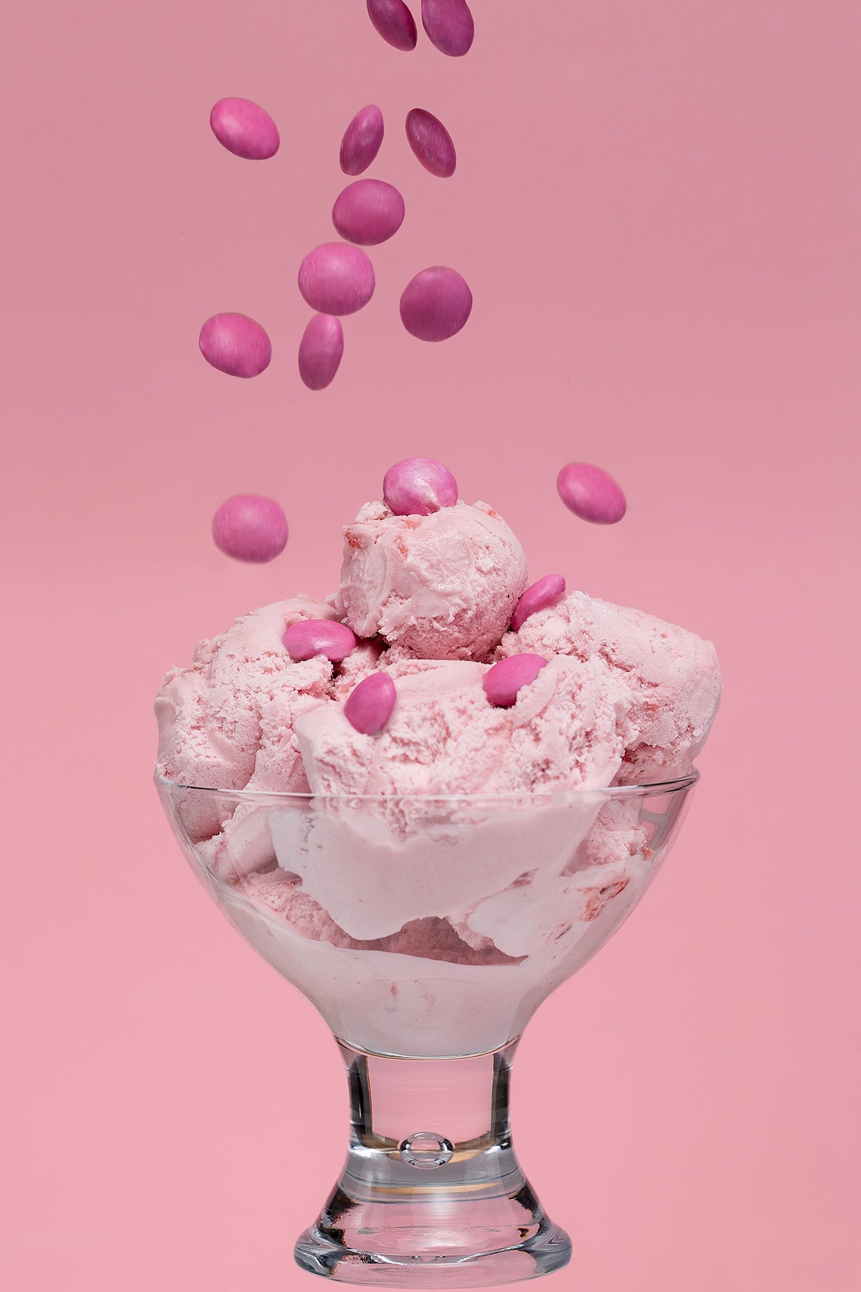 Pink ice cream with pink candies in a glass bowl on a pink background