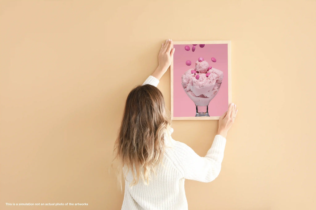 Person holding a framed picture of pink ice cream against a beige wall